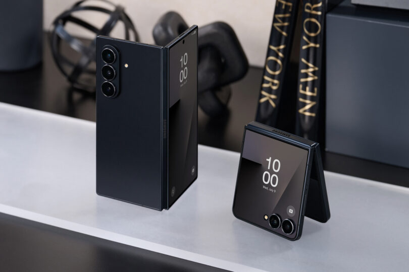 Zwei schwarze Samsung -Smartphones werden auf weißen und schwarzen Oberflächen angezeigt. Der eine entwickelt sich vertikal und der andere wird teilweise gefaltet, beide zeigen die digitale Uhr auf ihren Bildschirmen.