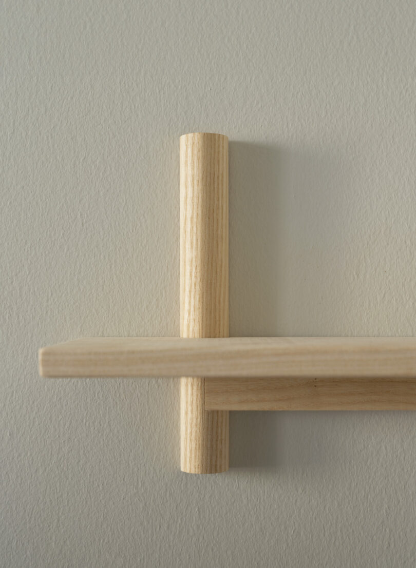 A minimalist wooden shelf is mounted on a light-colored wall, featuring simple, clean lines and a cylindrical vertical support