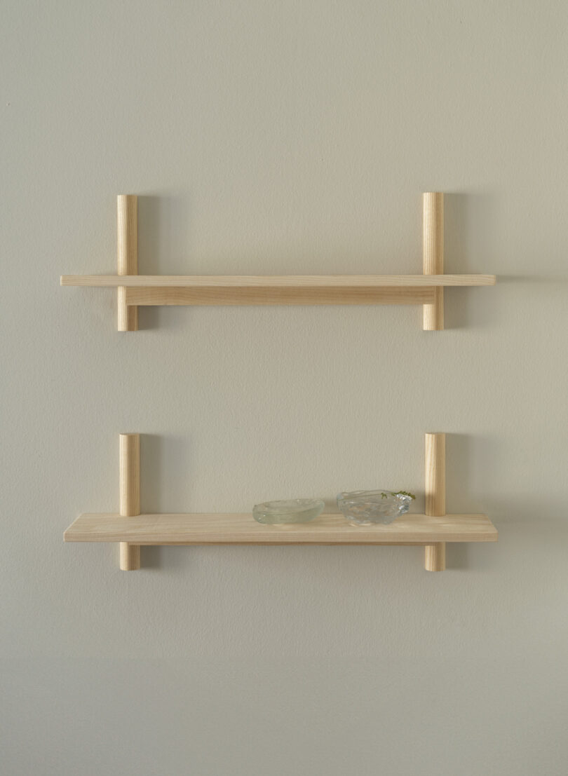 Two minimalist wooden wall shelves, the lower shelf holding two small glass bowls, mounted on a light-colored wall