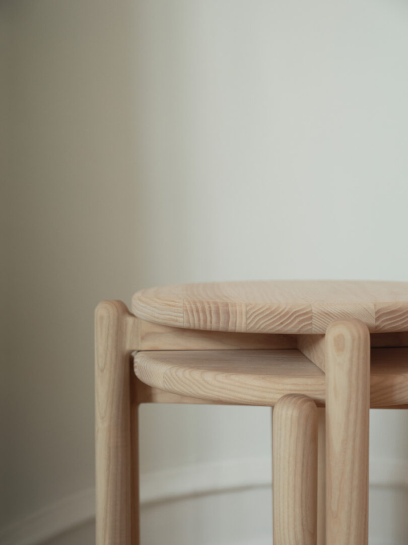 Two round, light wood nesting tables are stacked together against a plain, off-white wall