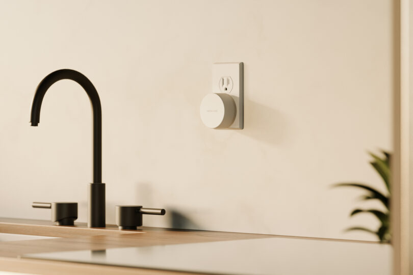 A TwelveSouth smart home device plugged into a wall outlet above a kitchen counter, with a modern black faucet and a small plant partially visible.