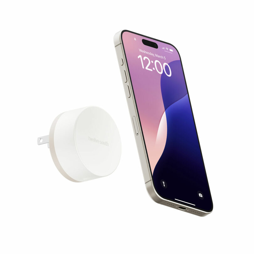 A smartphone floats next to a TwelveSouth white round wall charger with a foldable plug, both set against a plain white background.