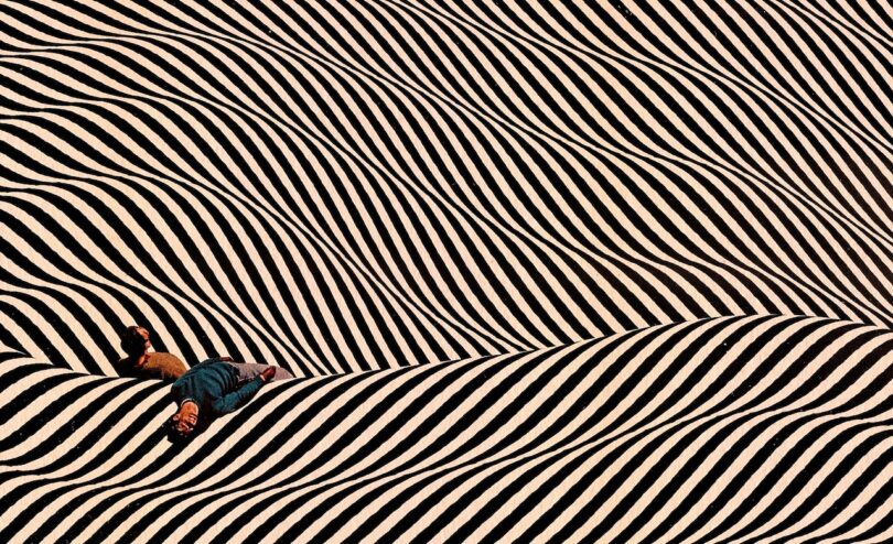 Die Person liegt auf der Oberfläche mit welligen schwarzen und weißen Streifen und erzeugt einen optischen Illusionseffekt