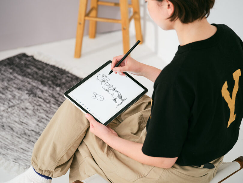 A person sitting and drawing a cartoon character on a tablet with a stylus.