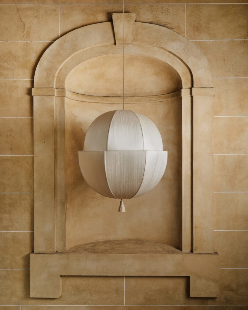 A spherical pendant light hangs in a recessed wall niche with an arched top and beige stone tiles.
