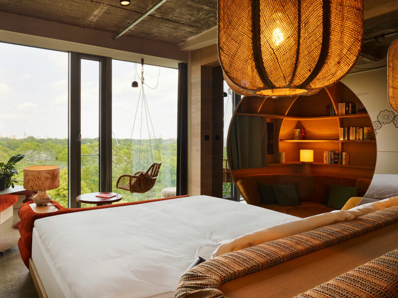 Modern bedroom with large windows, a swing chair facing greenery, and a bed in the foreground—plus a circular mirror reflecting a cozy 25hours-inspired reading nook with bookshelves.