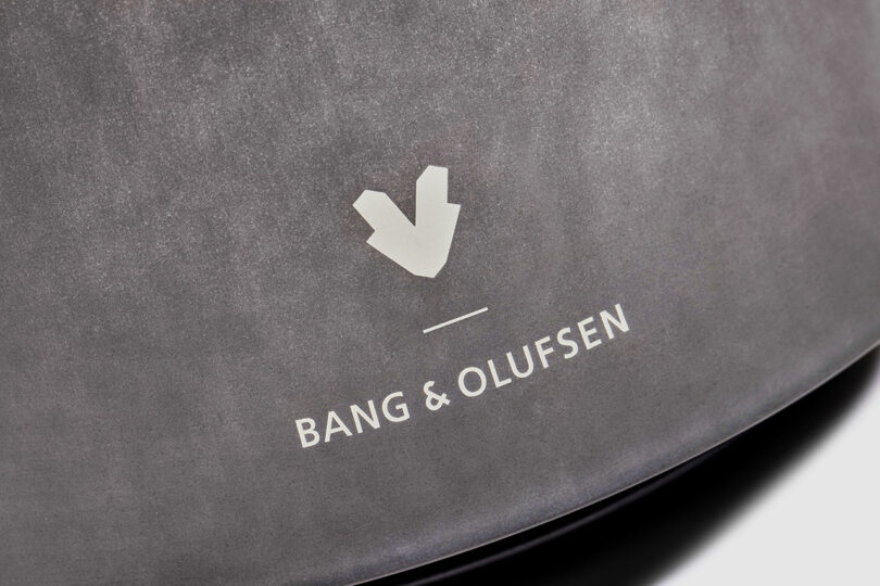 Close-up of the Bang & Olufsen logo printed in white on a matte gray surface, showcasing the brand's signature minimalist elegance.