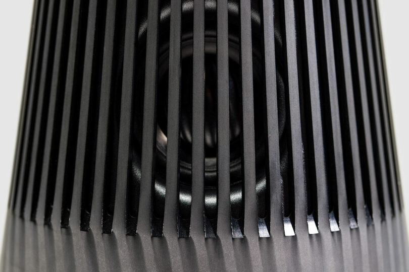 Close-up view of a Bang & Olufsen black speaker grill with vertical slats, revealing part of the speaker cone behind the grill.