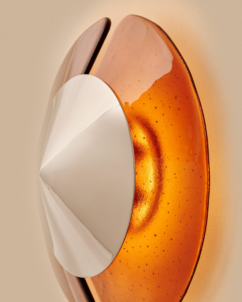 Close-up of a modern wall sconce featuring a metallic, cone-shaped center and amber-tinted glass panels emitting a warm light.