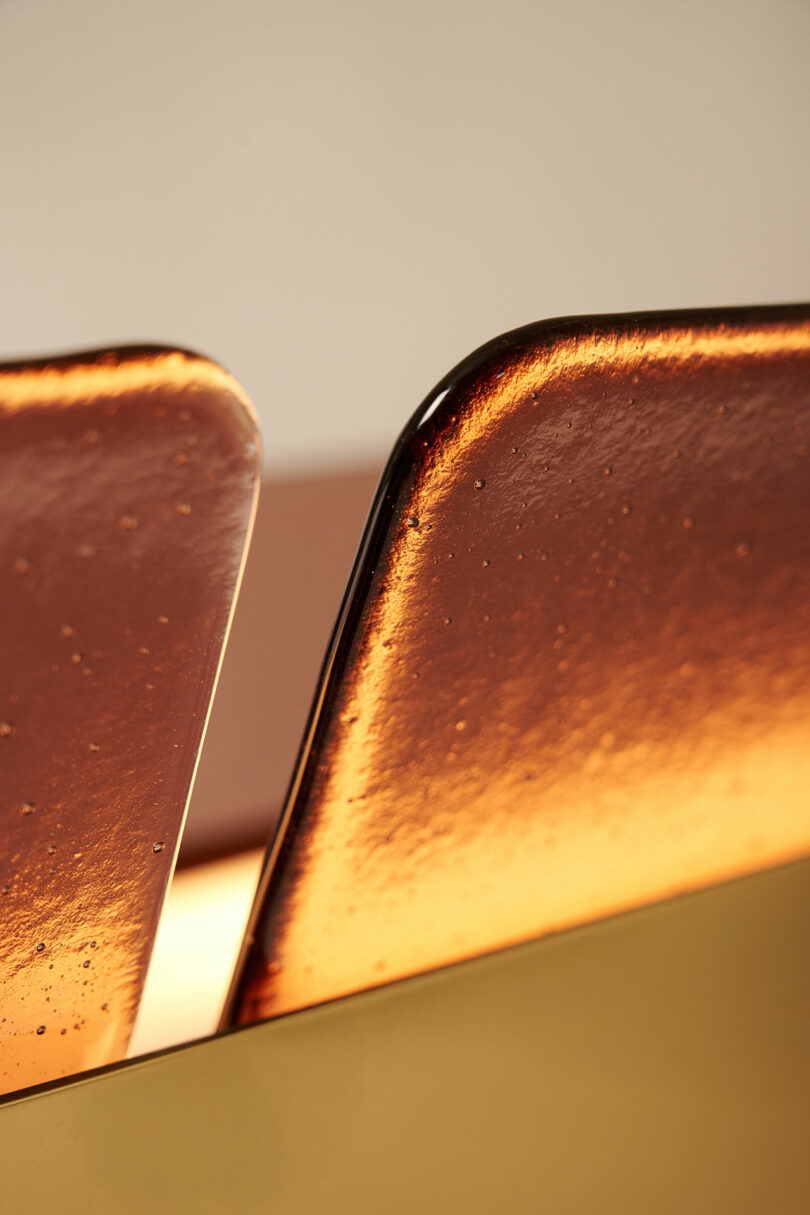 Close-up of two amber-tinted, textured glass or acrylic panels with rounded edges, illuminated by warm light and set against a neutral background.