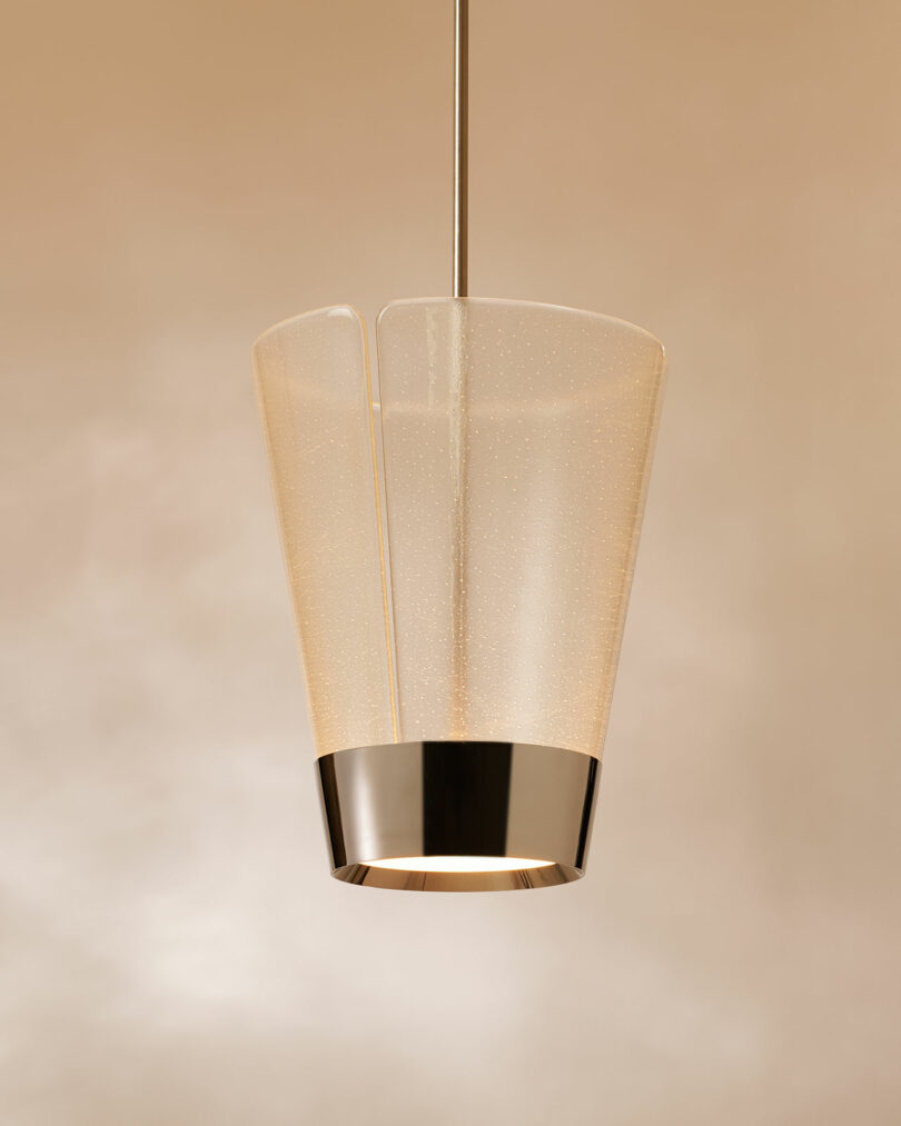 A modern pendant light fixture with a metallic base and a translucent, slightly flared glass shade, suspended against a neutral beige background.