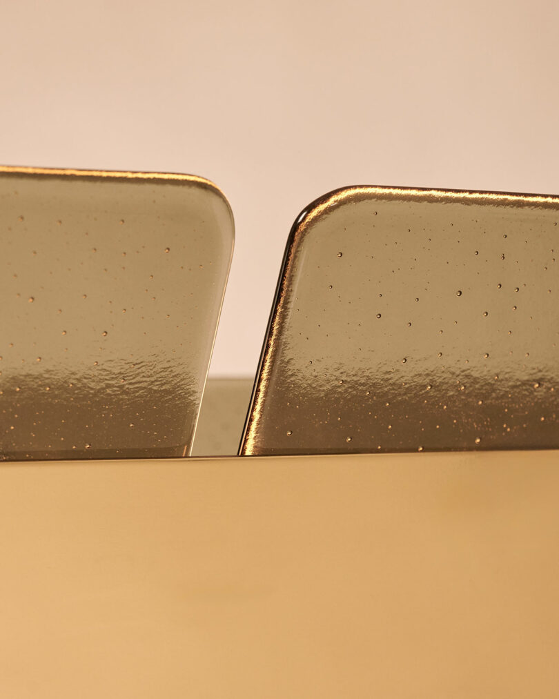 Close-up of two golden rectangular metallic objects with rounded edges, partially inserted into a golden surface, against a neutral background.