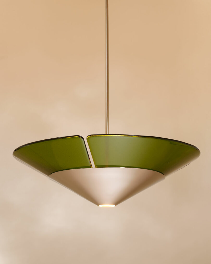 A modern pendant light fixture with a green, cone-shaped glass shade and a white diffuser, suspended from a metal rod against a beige background.