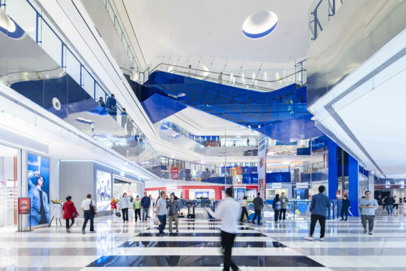 Spacious modern shopping center with great floors, glass fences, blue architectural accents and people who walk or buy.