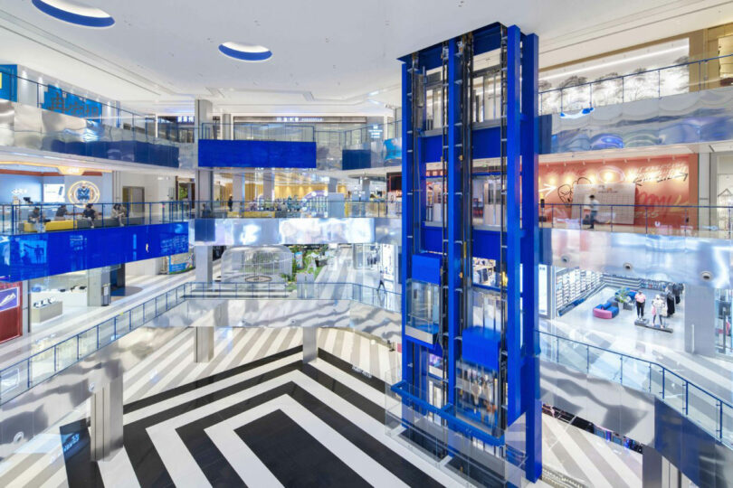 Interior of the modern shopping center with multiple levels, glass fences, blue glass lift and black and white striped floors.