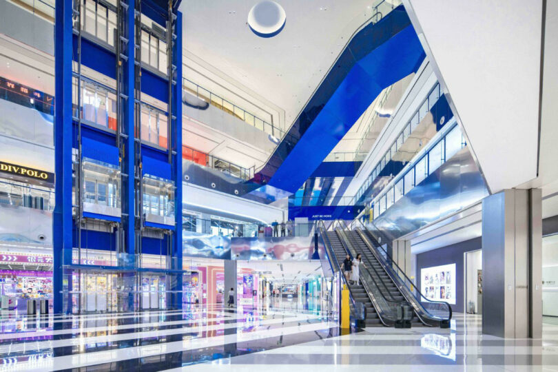 Contemporary shopping center Inland with great floors, blue escalators, glass elevator and various stores visible at several levels.