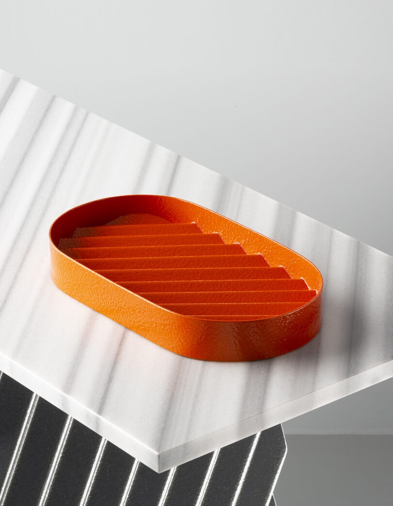 Una bandeja ovalada de textura naranja con el interior de la cámara de la cresta se coloca sobre una superficie de mármol blanco con venas grises.