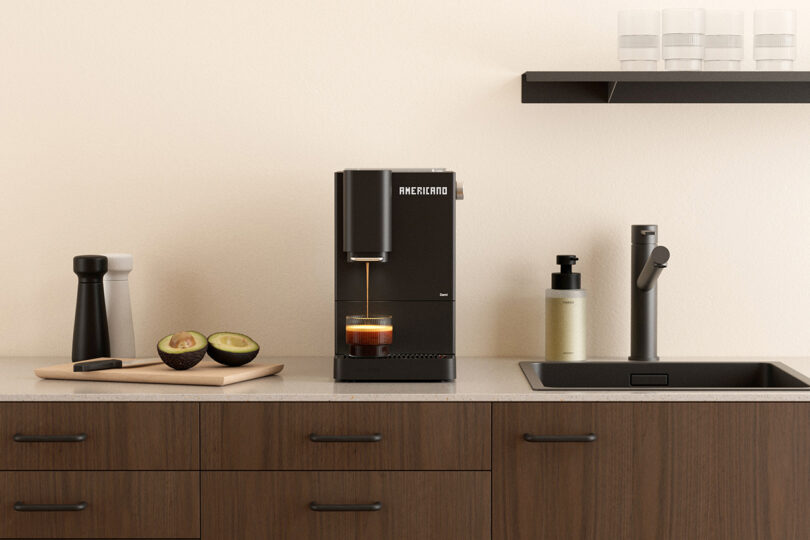 A modern kitchen counter with a coffee machine brewing coffee, a cutting board with sliced avocado, a pepper grinder, a soap dispenser, and a sink with a faucet.