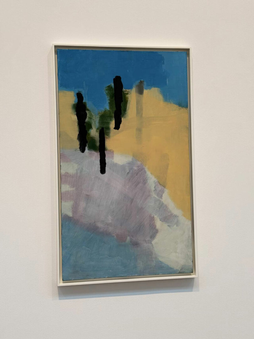A framed abstract painting by Maha Alavi featuring blocks of blue, yellow, and purple with vertical black shapes and green accents, displayed on a white wall.