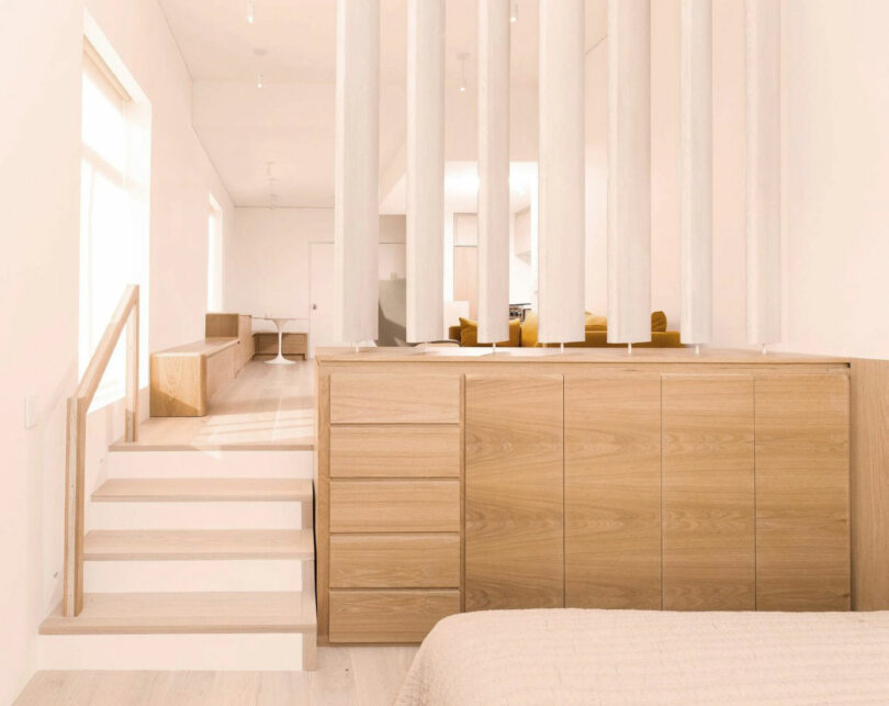 Minimalist bedroom Nicki Gitlin with a light wooden cabinet, vertical white weak as a split room and steps leading to a raised seated area bathed in natural light.