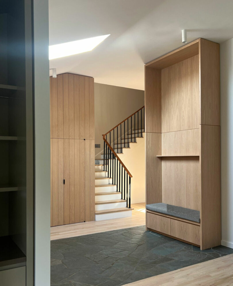 The modern input of Nicki Gitlin has a lightly wooden cabinet, built-in bench, noon and staircase with elegant black fences leading up.