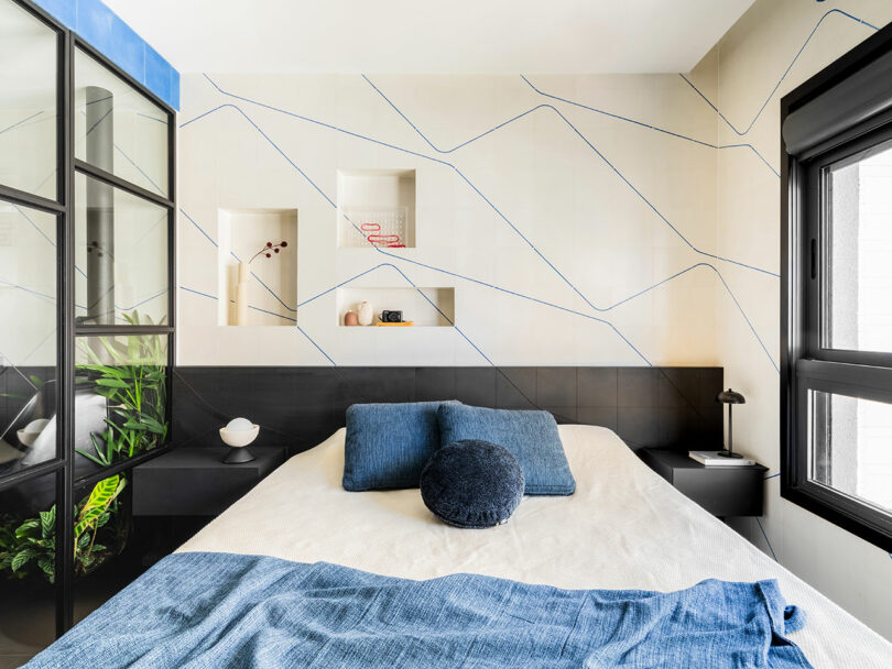 Dormitorio moderno con una cama contra una pared de acento geométrico, estantes incorporados, partición de vidrio enmarcado negro y grandes ventanas que dejan luz natural.