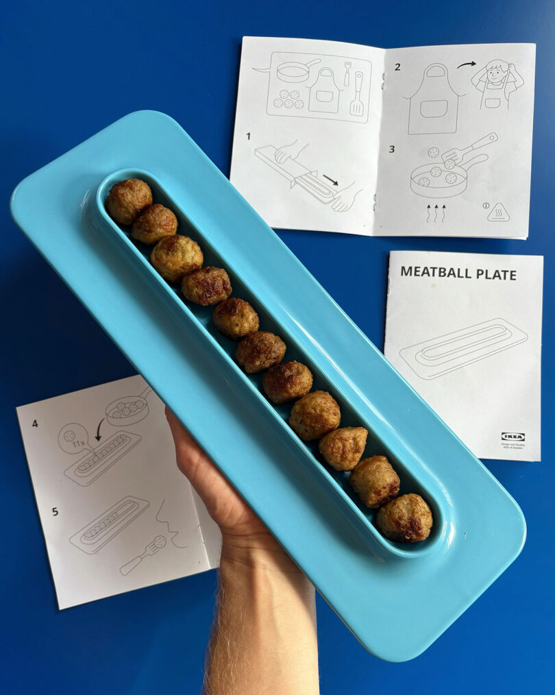 Hand keeps the blue plate with a series of meat districts; IKEA instructions in the style are displayed on a blue table in the background.