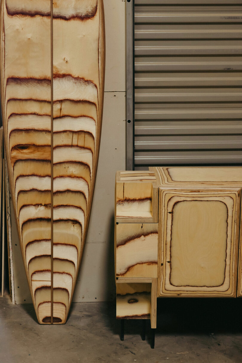 Ein Holz -Surfbrett und ein Holzschrank mit entsprechenden natürlichen Verbrennungsmustern, die an den Kelly Wearstler Signature -Stil erinnern, steht neben der Metallgarage in der inneren Umgebung.