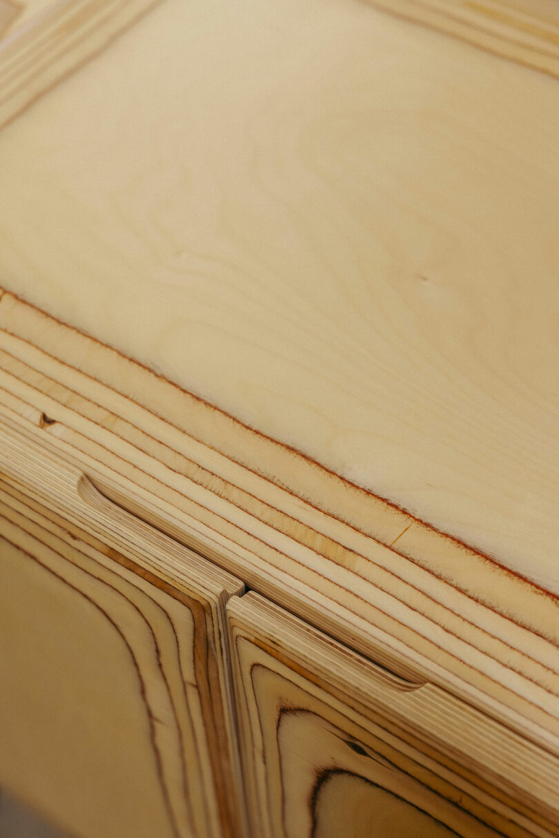 Eine detaillierte Sicht auf die hellgeläutete Holzoberfläche mit sichtbaren laminierten Kornmustern und glatten, abgerundeten Kanten, ein widerspenster Stil, der häufig in den raffinierten Kelly Wearstler -Innenräumen beobachtet wird.