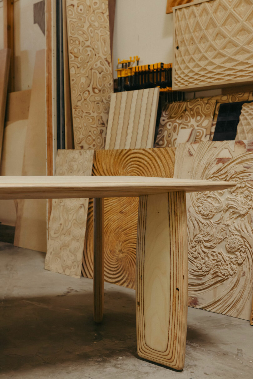 Der Holztisch steht in der Werkstatt, umgeben von verschiedenen komplexen, geschnitzten Holzplatten und präsentiert einen Stil, der an die mutigen und künstlerischen Designs von Kelly Wearstler erinnert.