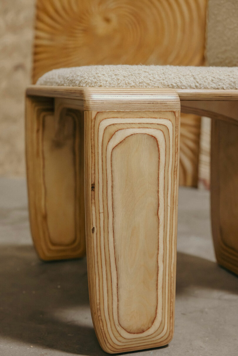 Detail eines hölzernen Stuhls mit sichtbaren Holzmustern und einem gepolsterten Sitz, inspiriert von Kelly Wearstler, eingebaut im Hintergrund mit ähnlichen Holztexturen.