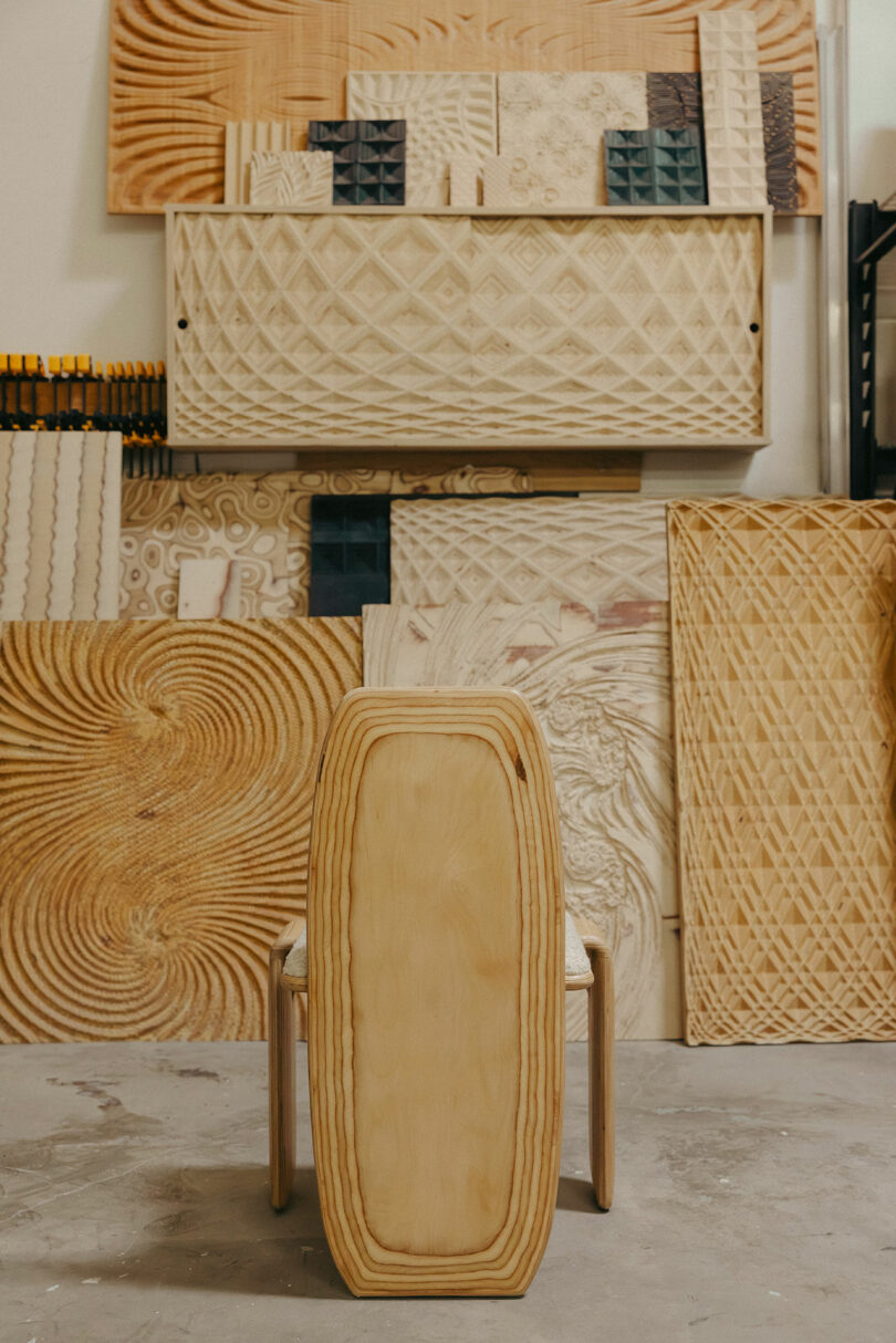 Der Holzstuhl steht vor mehreren geschnitzten und gemusterten Holzpaneele und ruft die Ästhetik hervor, die von Kelly Wearstler in der sonnenverrückten Workshop inspiriert sind.