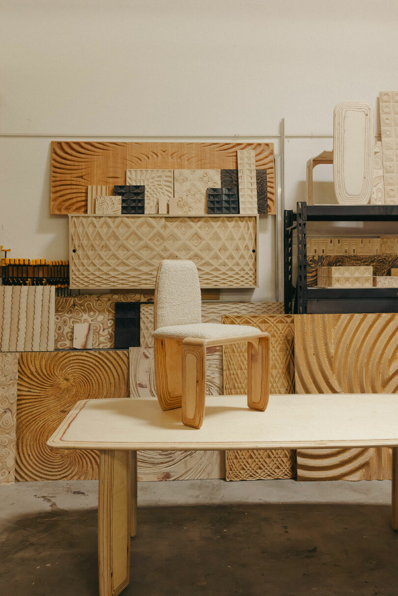 Der Holztisch verfügt über einen modernen Holzstuhl mit einem gepolsterten Sitz, ergänzt durch geschnitzte Holzpaneele, die in den Regalen und gegen die Wand angeordnet sind, und ruft Ästhetik hervor, die von Kelly Wearstler inspiriert sind.