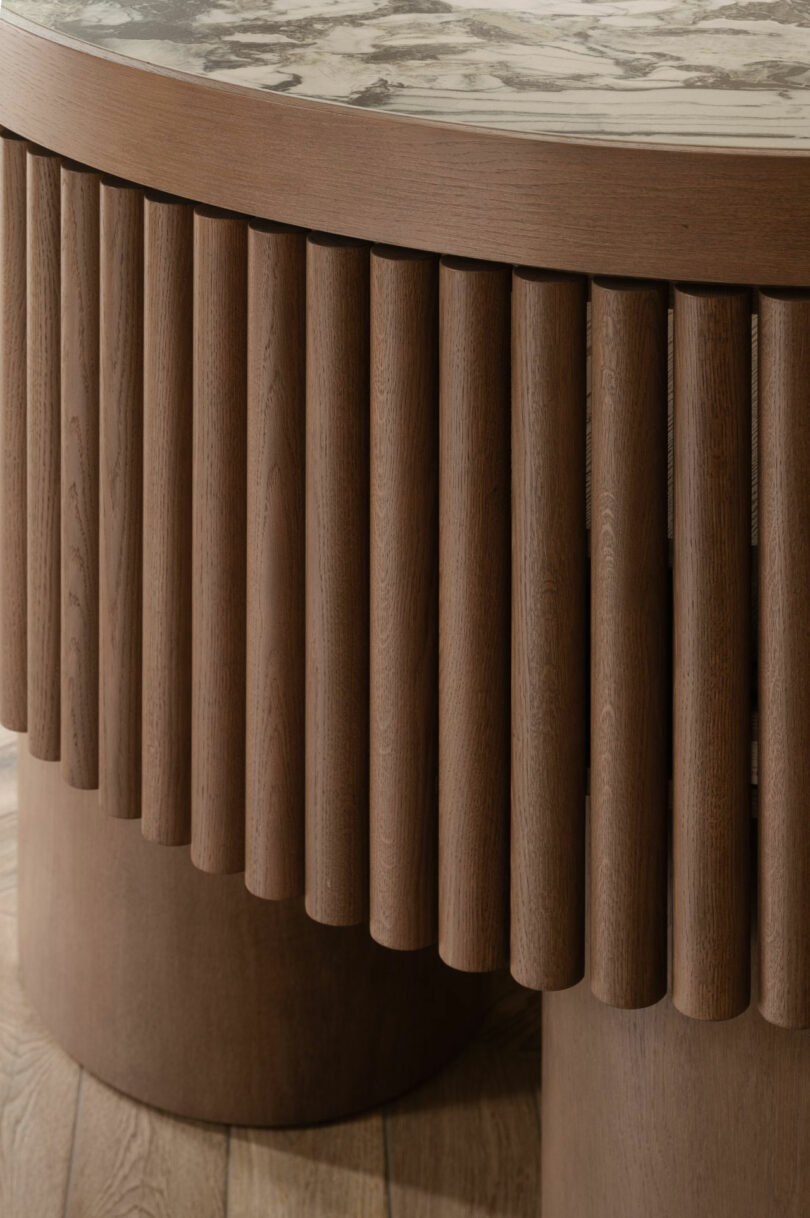 Primer plano de la mesa de madera con paneles cilíndricos verticales y mesa de mármol circular en el piso de madera.