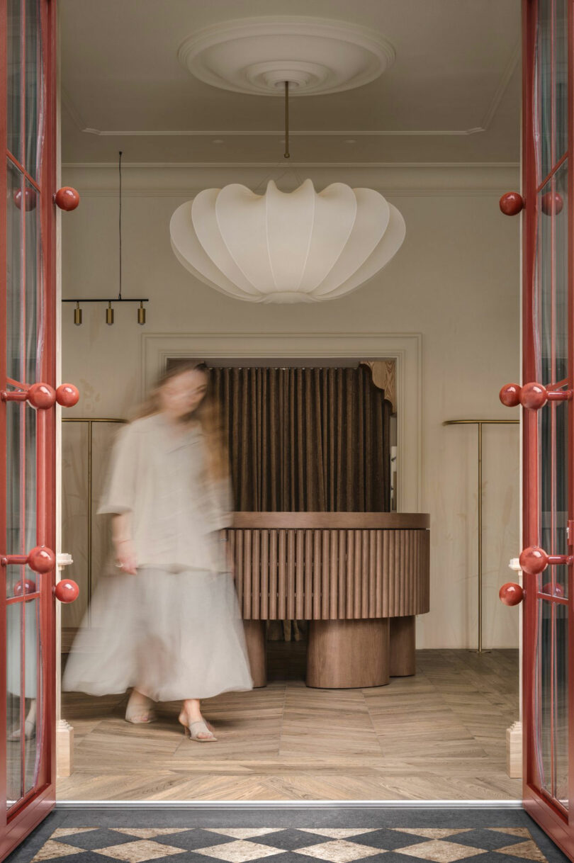 Un hombre con ropa ligera borraba al hombre caminando en una habitación con muebles de madera, grandes candelabros y puertas dobles de marco rojo.
