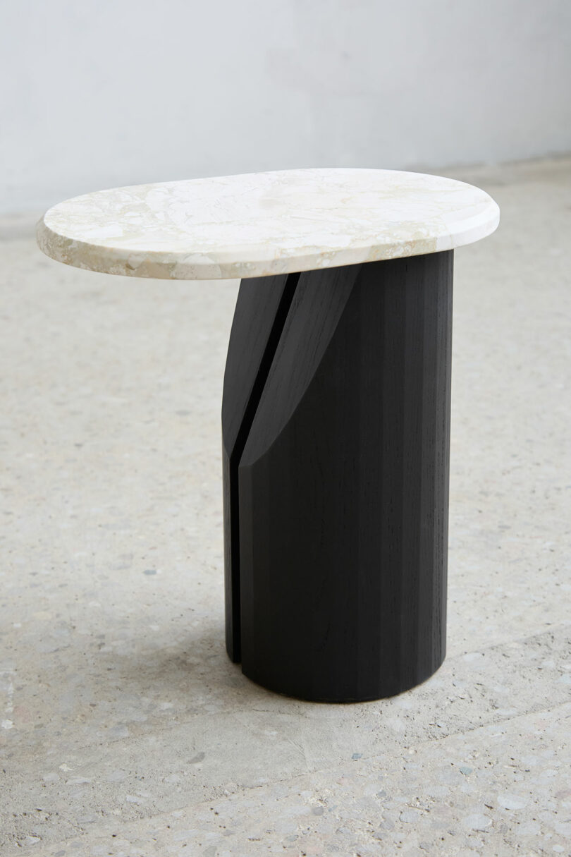 Small side table with white, oval marble and cylindrical black wooden base with vertical grooves.