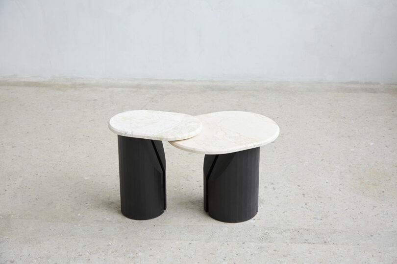 Two modern side tables with round, white marble tops and cylindrical black databases were placed next to each other on light, stains on a semicircle on the plain wall.