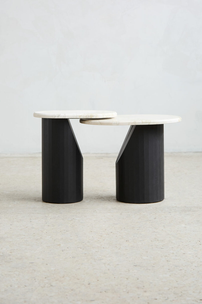 Two modern side tables with round white tops and cylindrical black databases were placed next to each other on the pity of light coloring on the plain wall.