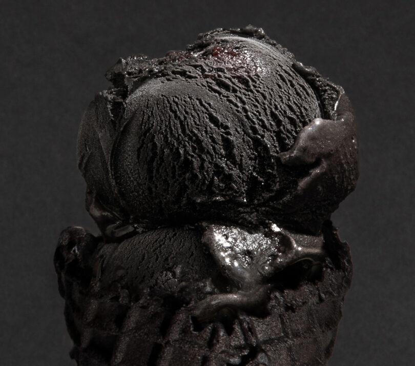 Close-up of a black ice cream scoop on a black waffle cone against a dark background.