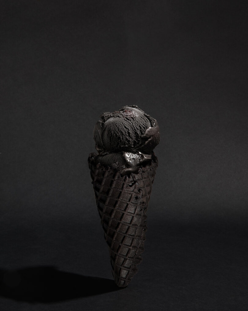 A black ice cream cone with a scoop of black ice cream, set against a dark background.