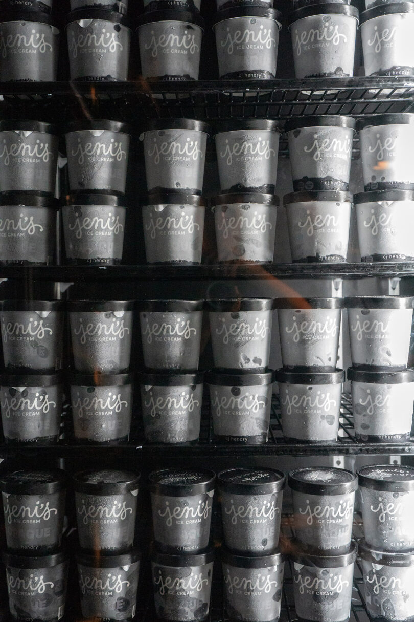 Multiple shelves stocked with pints of Jeni's Splendid Ice Creams, arranged in rows inside a freezer, evoke the OPAQUE CJ Hendry aesthetic—a harmonious blend of vibrant color and precise organization.