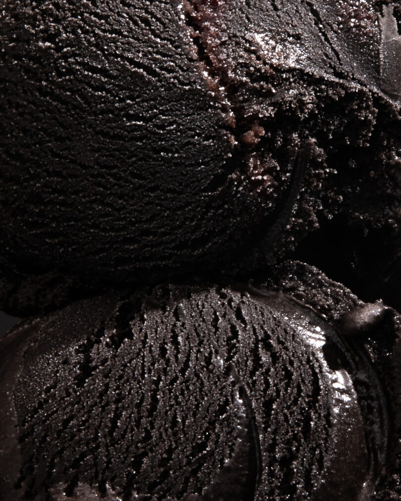 Close-up of two scoops of dark chocolate ice cream, showing textured, creamy surface and rich, dark color.