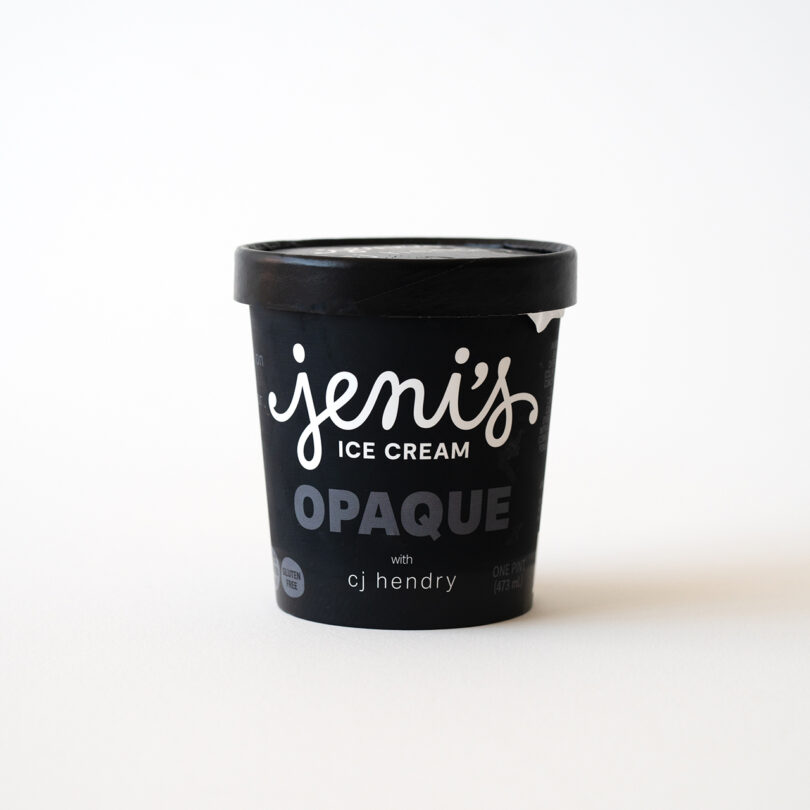 A black pint container of Jeni’s Ice Cream labeled “OPAQUE with cj hendry” sits on a white surface with a plain background.