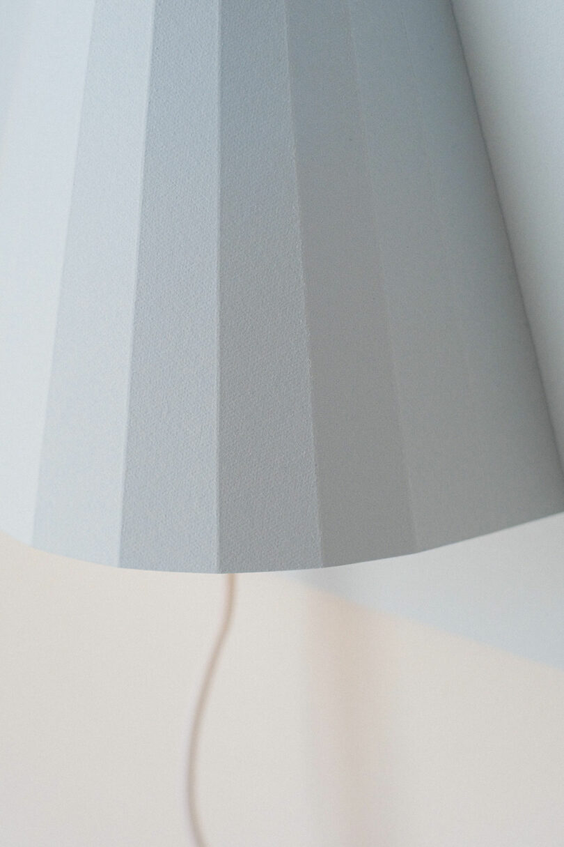 Close-up of a light gray, textured lampshade with a pleated design, with a white cord visible in the background.