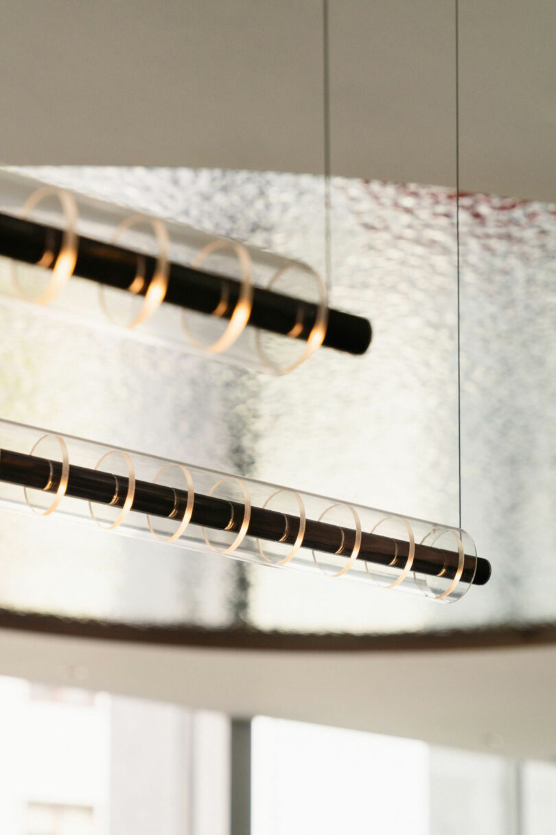 Two modern coloring light fixings with cylindrical glass shades and visible spiral filaments hang from the ceiling in modern interior.