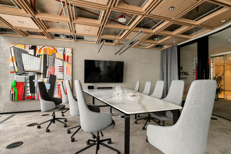 Modern conference hall with a long white table, gray turntables, large wall screen, abstract art and wooden ceiling.
