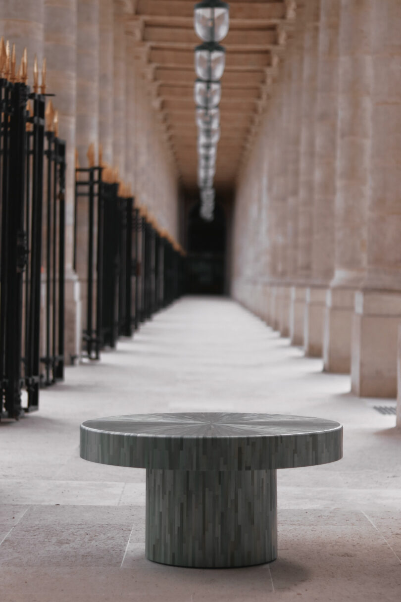 A round, modern stone table is positioned in a covered outdoor walkway with columns and hanging lights.