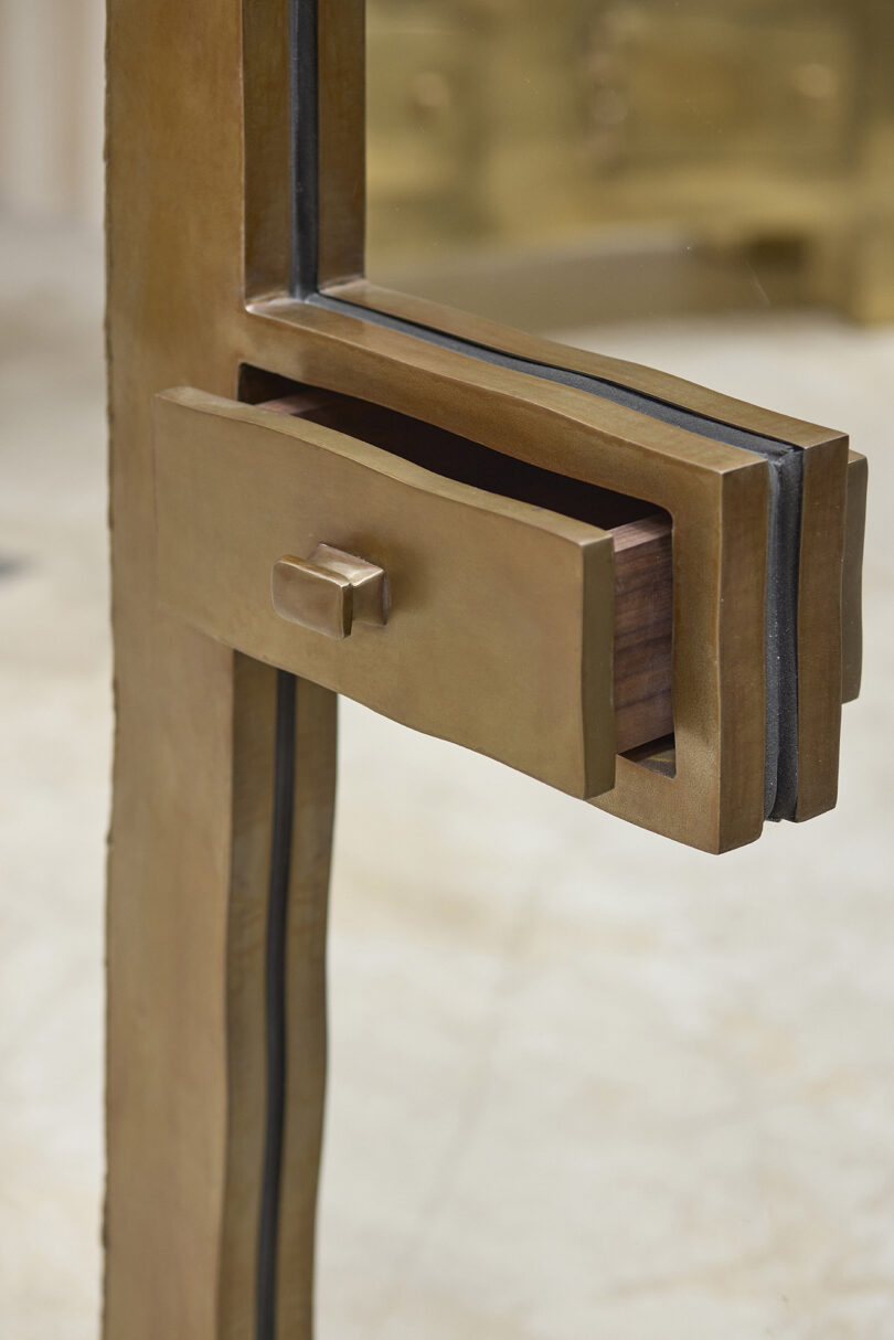 Close-up of a bronze structure featuring a rectangular drawer partially open, integrated into the frame, with a blurred background.