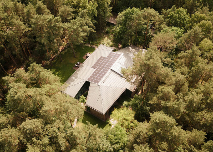 A house surrounded by dense trees, seen from above, with solar panels installed on its roof.
