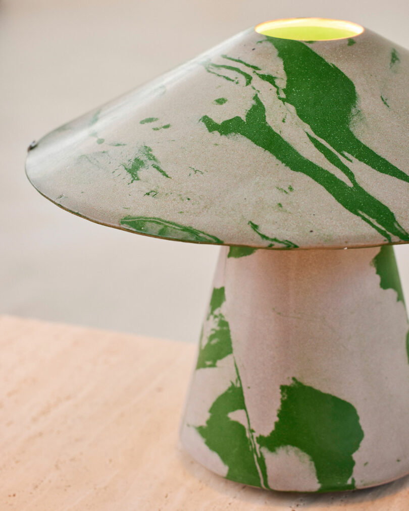 A ceramic mushroom-shaped lamp from Upglas Luca Nichetto, featuring a marbled green and gray pattern, sits on a light-colored surface.